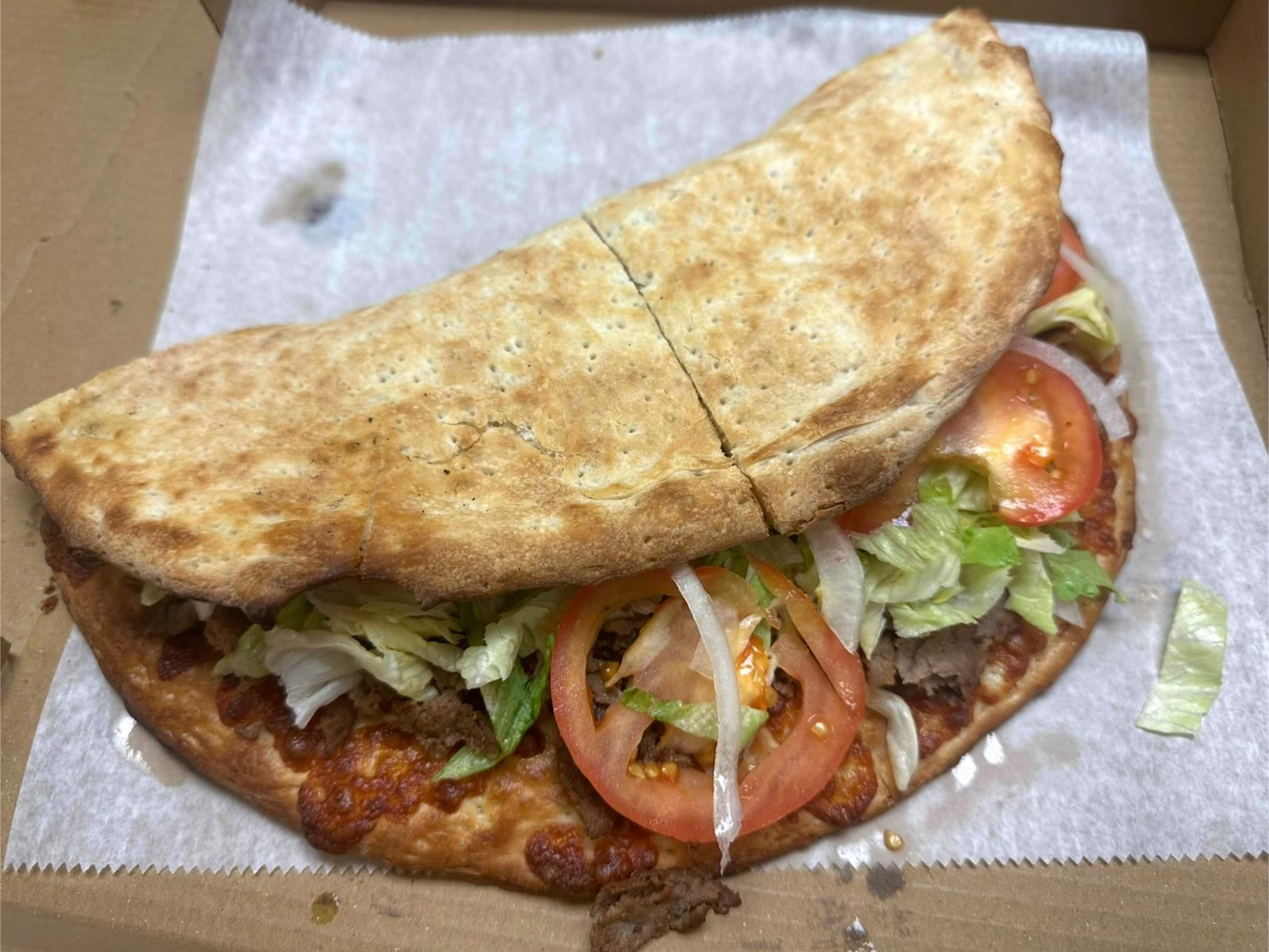 Calzone sandwich with lettuce, tomato, and onion in a cardboard box.