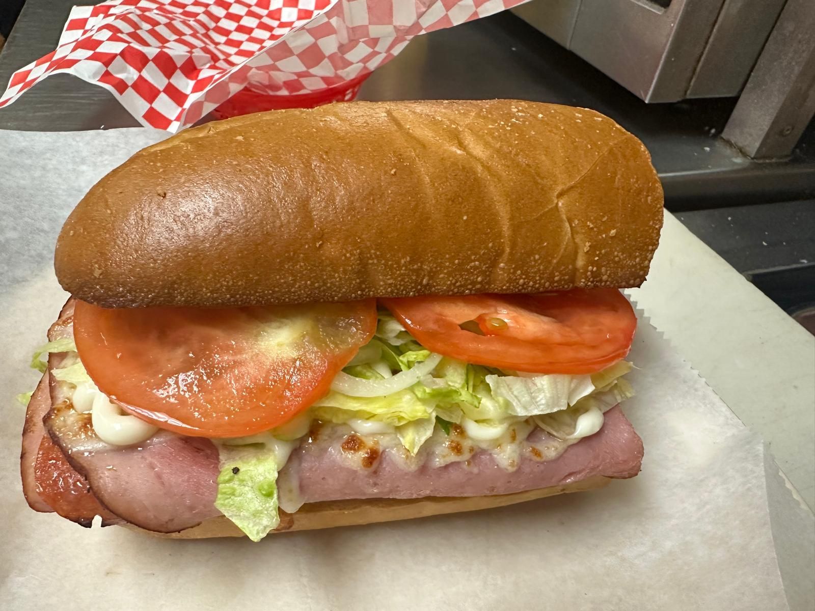 Submarine sandwich with ham, tomato, lettuce, and mayo on a bun, placed on paper.