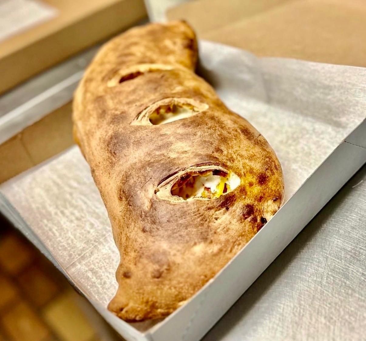 Calzone in a pizza box, golden brown crust with visible filling peeking through openings.