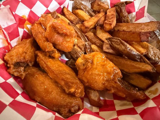 Chicken wings and potato wedges in a red and white checkered basket.