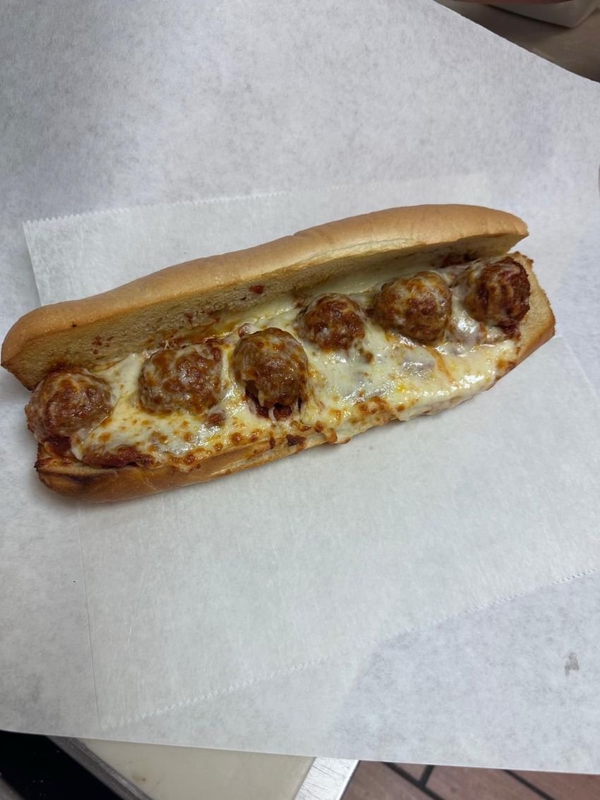 Meatball sub with melted cheese on a lightly toasted bun, served on white paper.