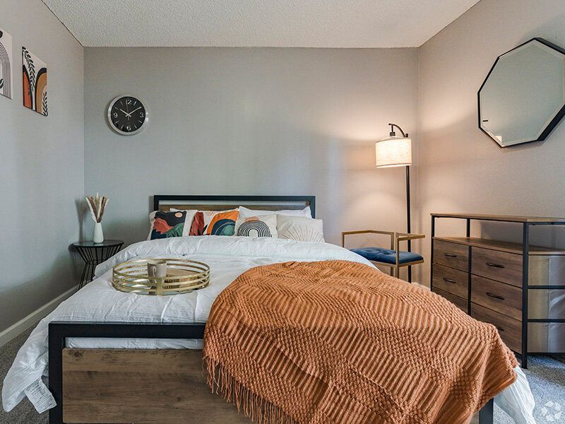 Bedroom in a modern apartment with a bed, dresser, and orange throw at Reno Vista Apartments.
