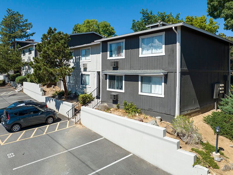 Exterior view of a gray two-story apartment building with white trim and a parking lot at Reno Vista Apartments.