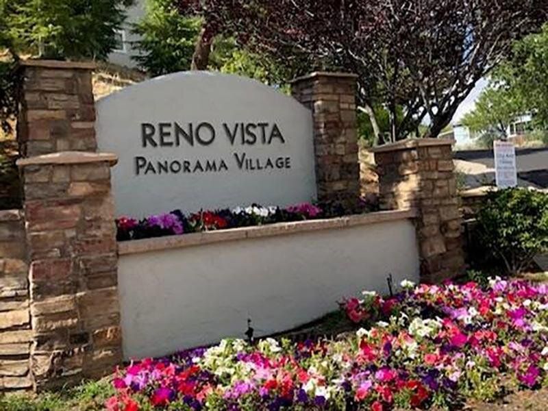Entrance sign reading Reno Vista Panorama Village with stone pillars and colorful flowers at Reno Vista Apartments.