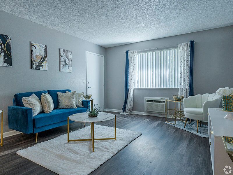 Living room in an apartment with a blue sofa, white chairs, and a marble coffee table near a window at Reno Vista Apartments.