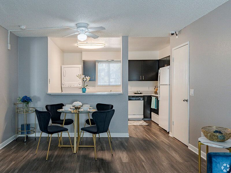 Open-concept apartment kitchen and dining area with round glass table and four blue chairs at Reno Vista Apartments.