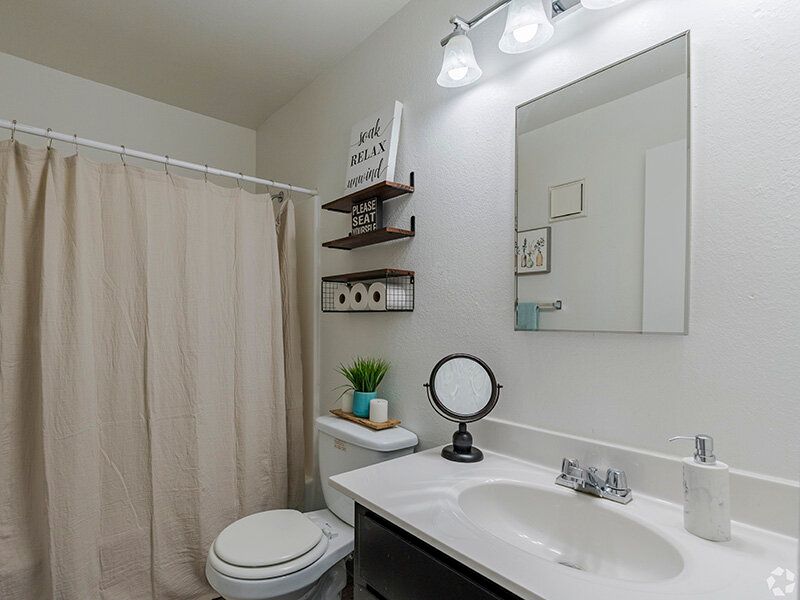 Bathroom in apartment with sink, mirror, toilet, and beige shower curtain at Reno Vista Apartments.