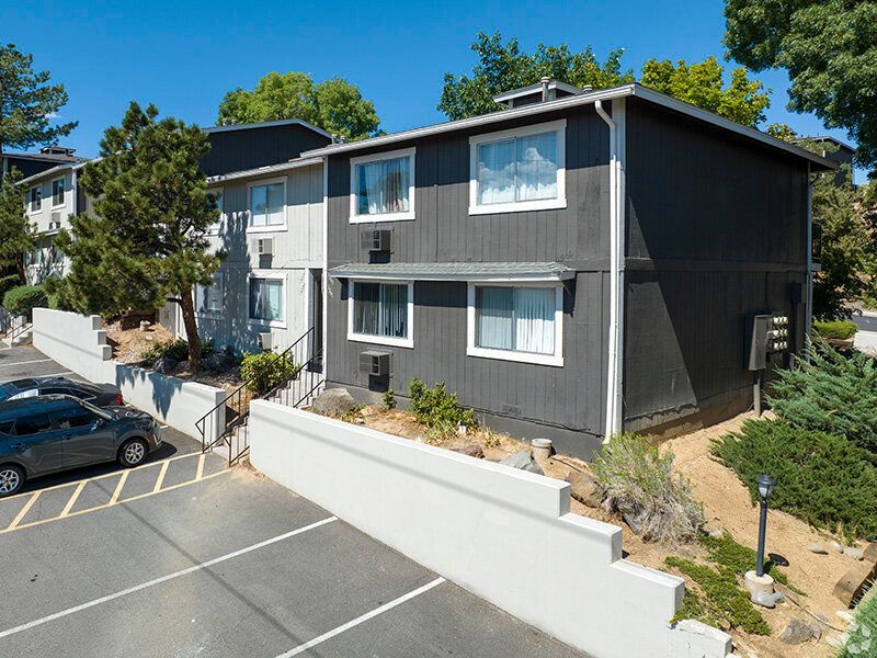 Two-story dark-gray apartment building with white-trimmed windows and a parking area at Reno Vista Apartments.