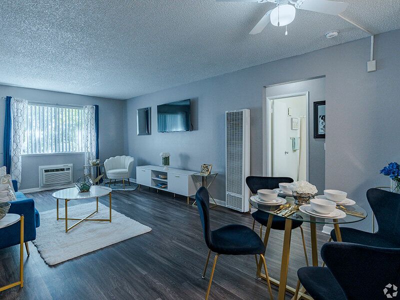 Living room with furniture, including sofa, chairs, table, and TV; gray walls and dark flooring at Reno Vista Apartments.