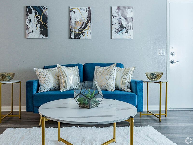 Bright living room with a blue sofa, geometric throw pillows, and a round marble coffee table at Reno Vista Apartments.