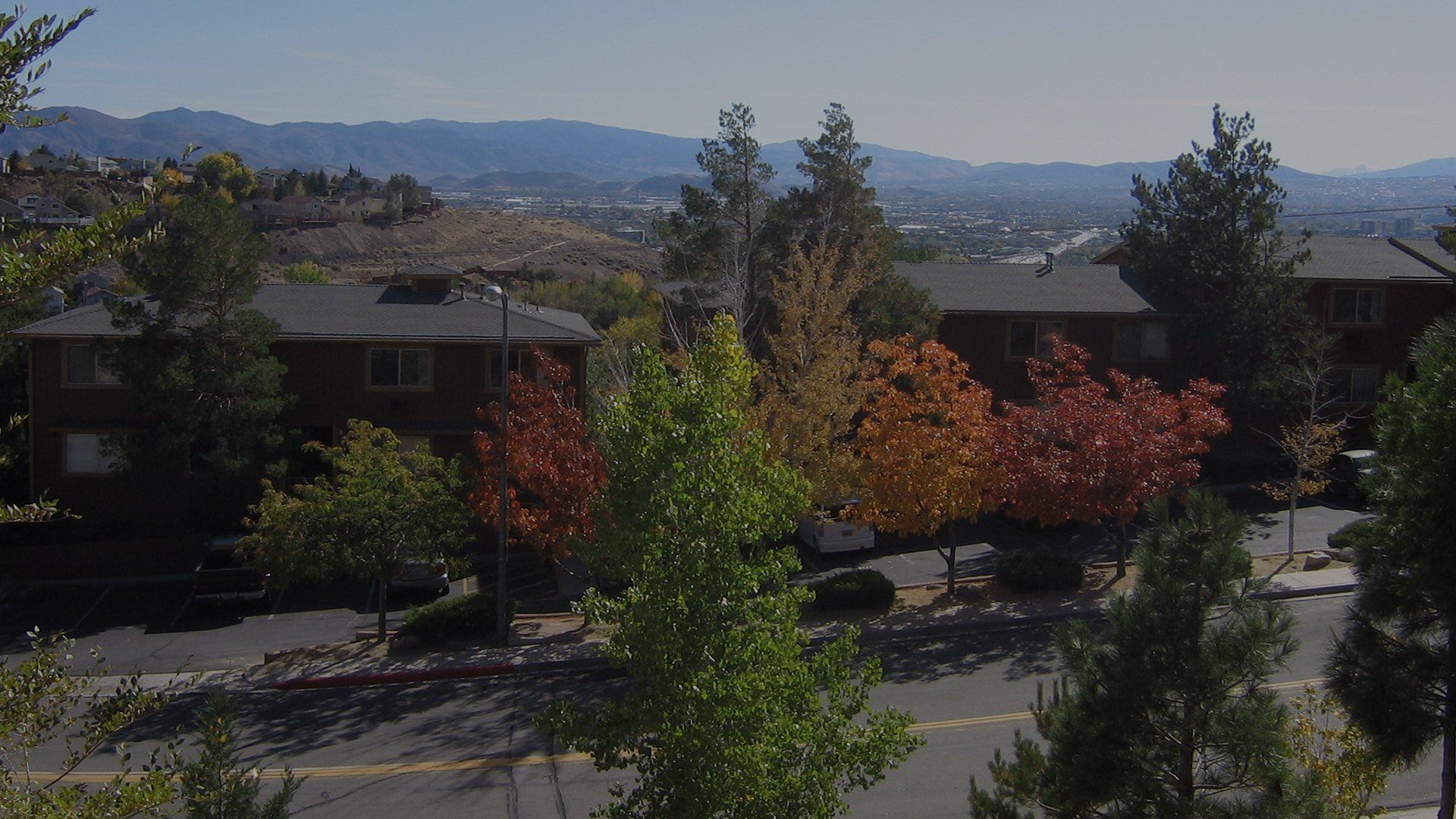 Exterior view of a multi-unit apartment complex with trees and distant hills at Reno Vista Apartments.