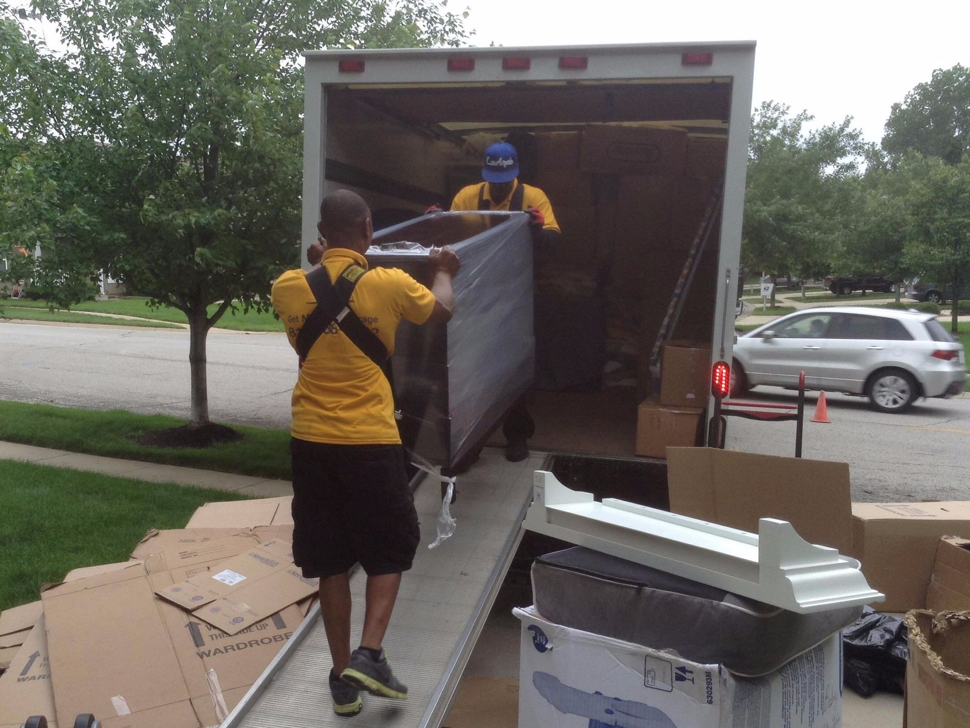 A man in a yellow shirt is carrying a large item out of a truck