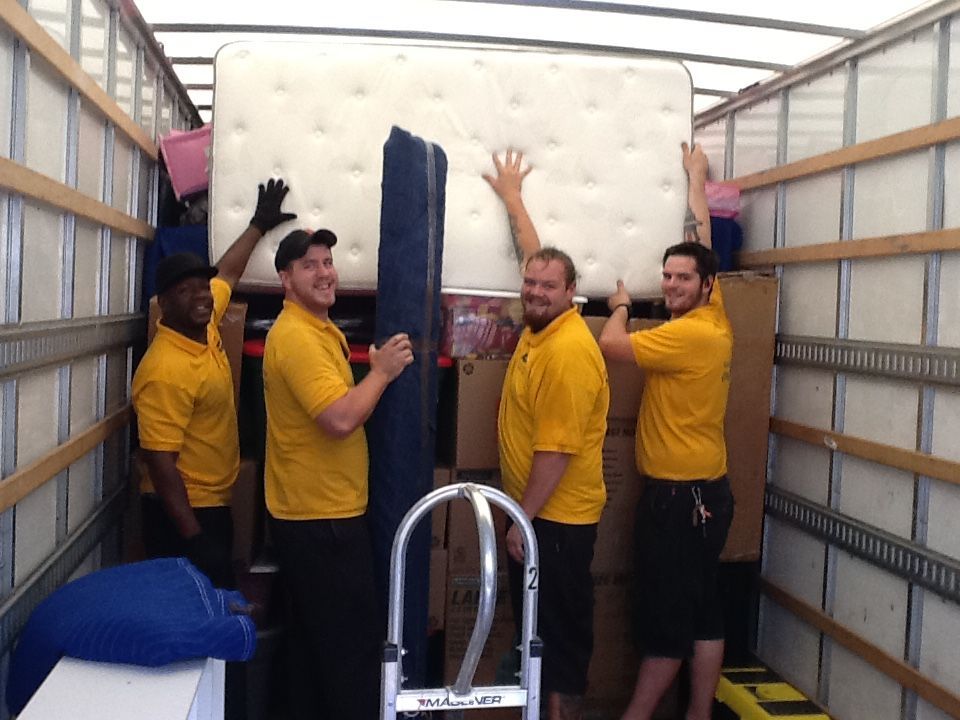 A group of men in yellow shirts are carrying a mattress in a truck