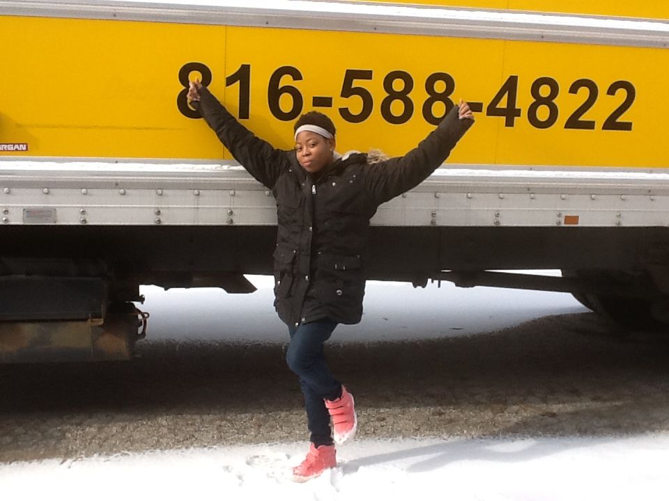 A girl leans against a yellow truck with the number 818-588-482 on it