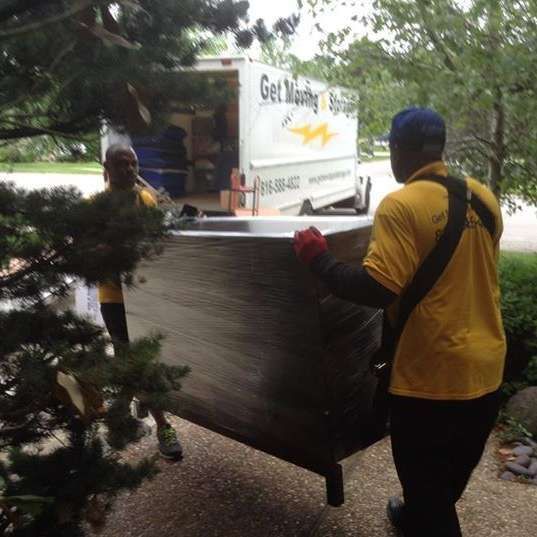A man in a yellow shirt is carrying a large piece of metal.