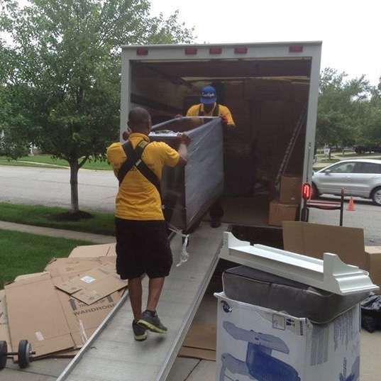 A man in a yellow shirt is carrying a piece of furniture into a truck