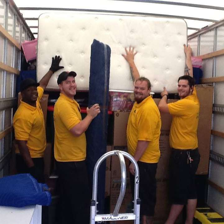 A group of men in yellow shirts are carrying a mattress in a truck