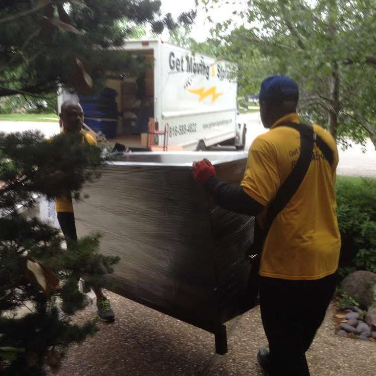 A man in a yellow shirt is carrying a large item in front of a get moving truck