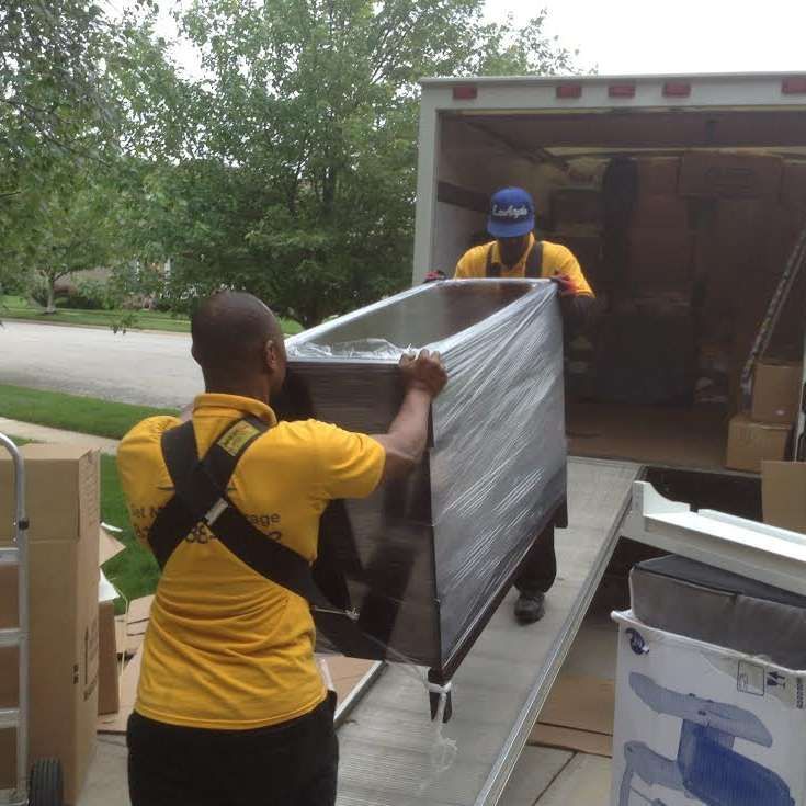 A man in a yellow shirt is carrying a large box