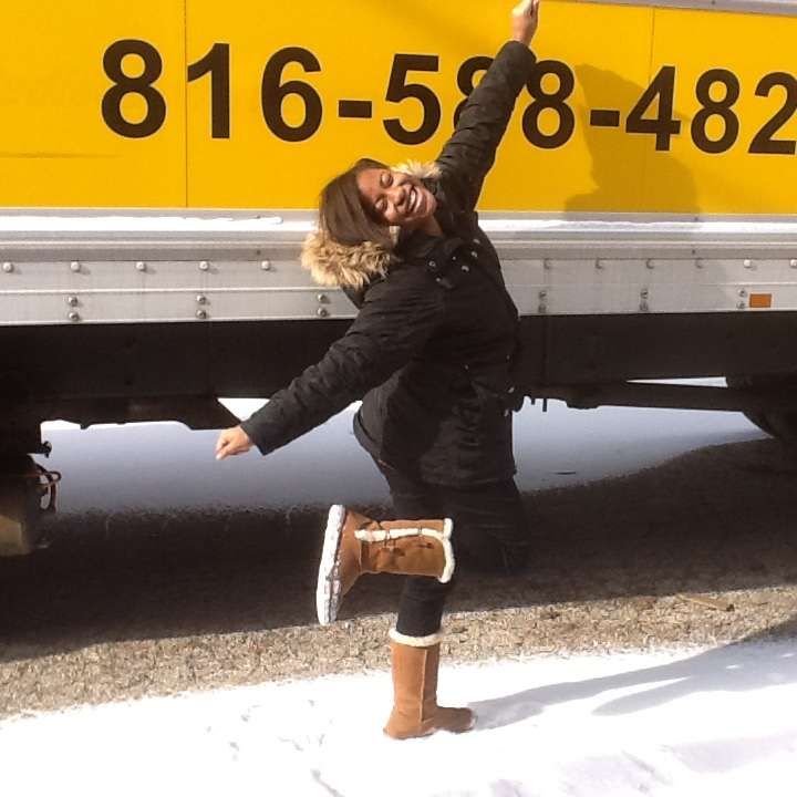 A woman stands in front of a yellow truck that says 818-598-483