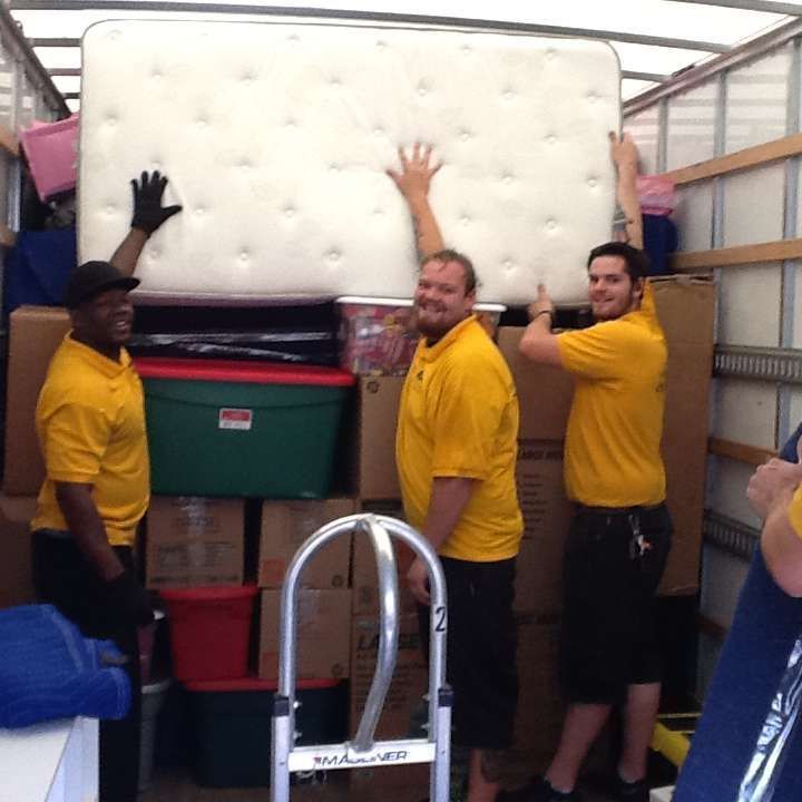 A man in a yellow shirt is carrying a mattress