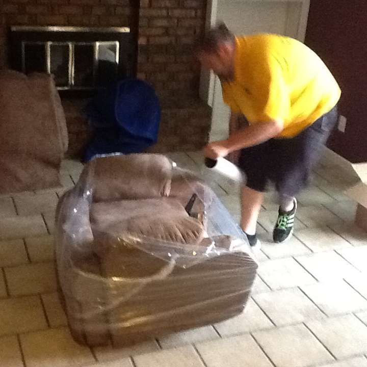 A man in a yellow shirt is standing next to a chair wrapped in plastic