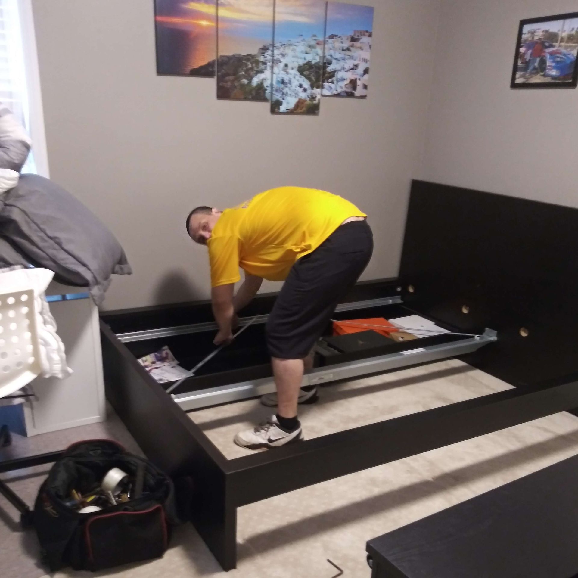 A man in a yellow shirt is working on a bed frame