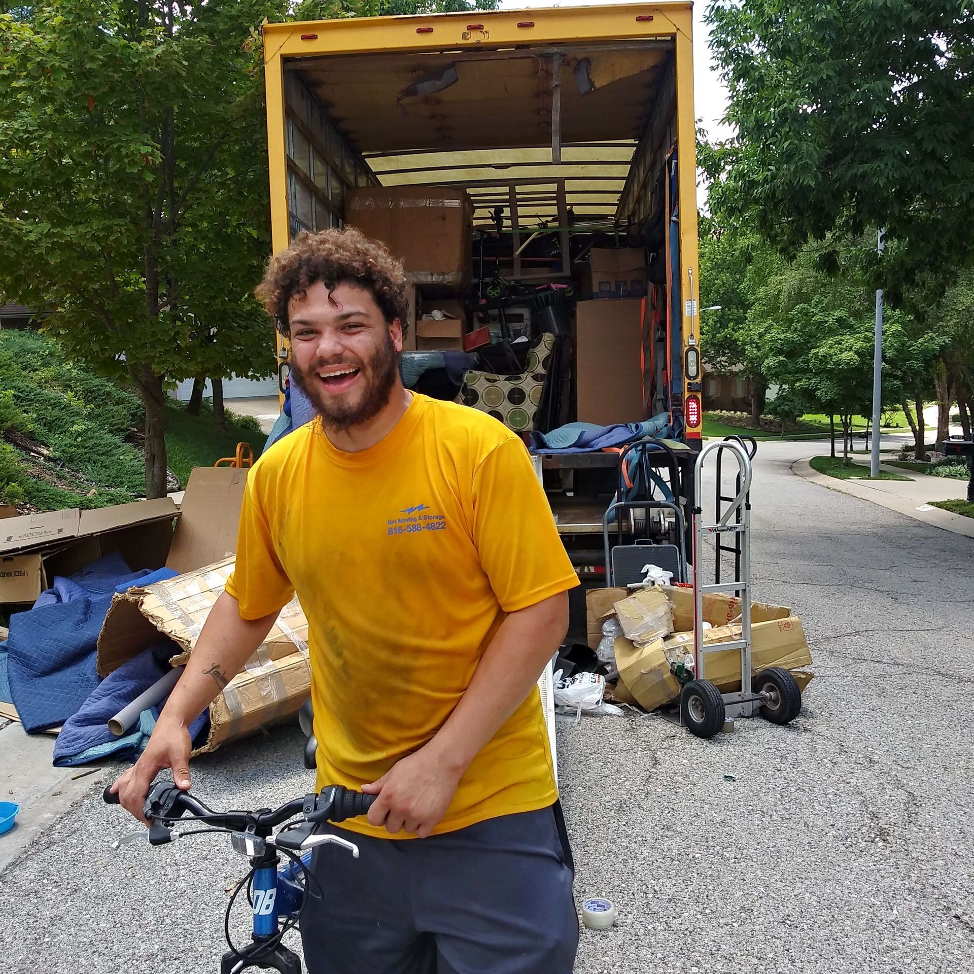 A man in a yellow shirt is holding a bike in front of a moving truck