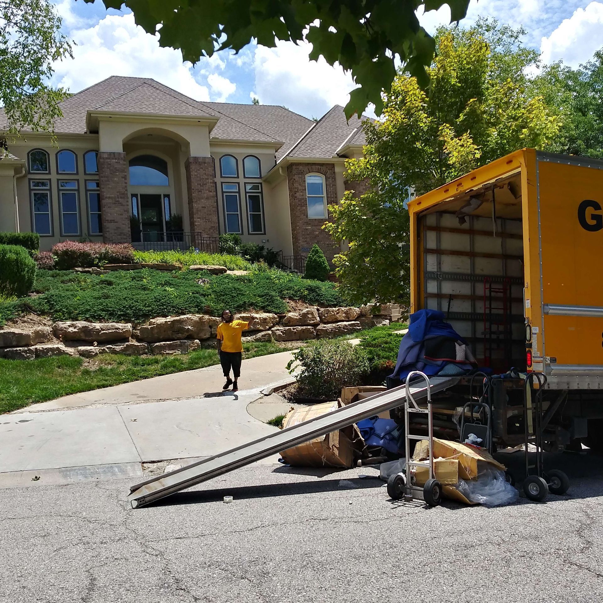 A yellow moving truck with the letter g on the side is parked in front of a house
