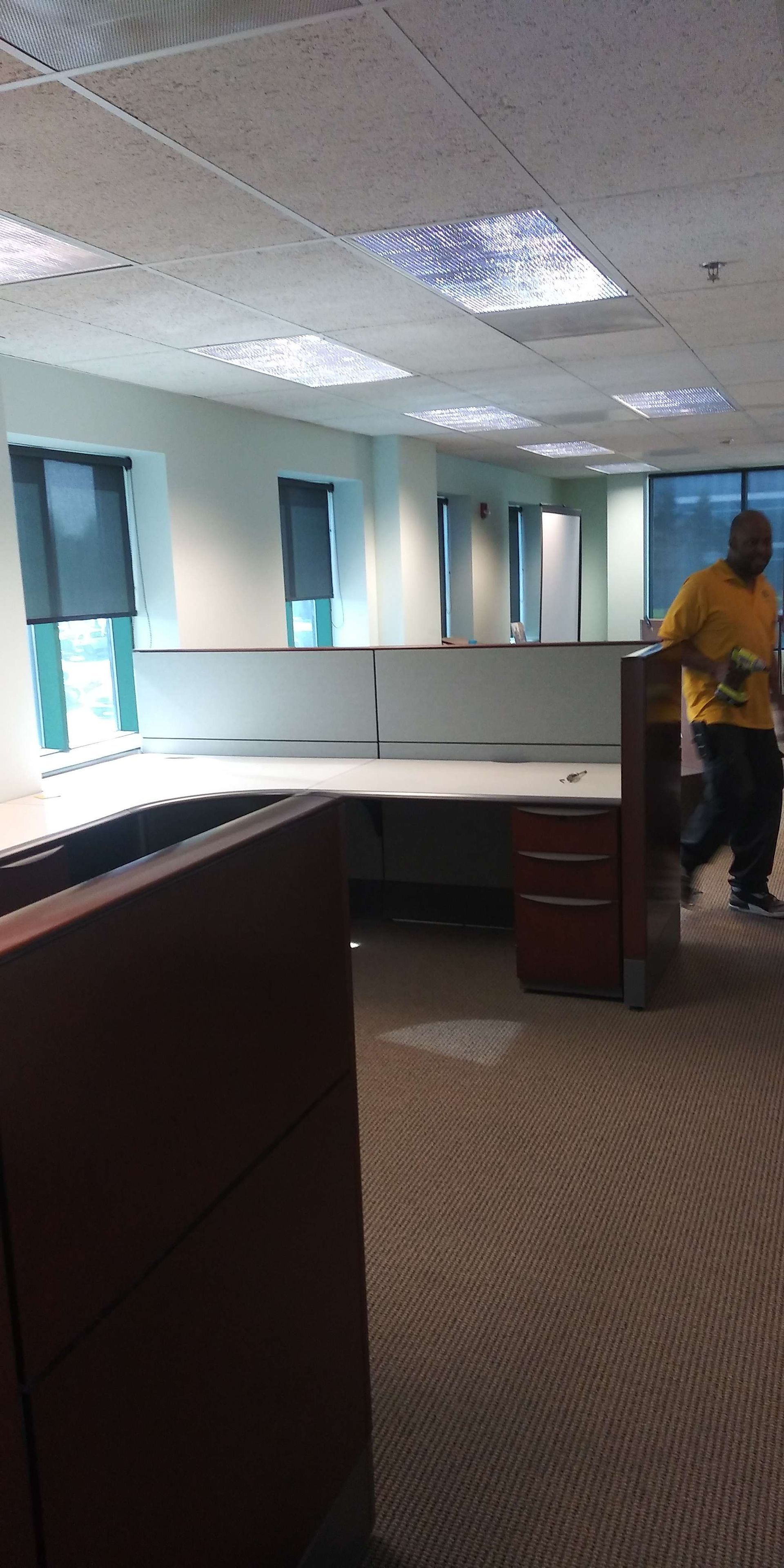 A man in a yellow shirt is standing in an empty office cubicle.