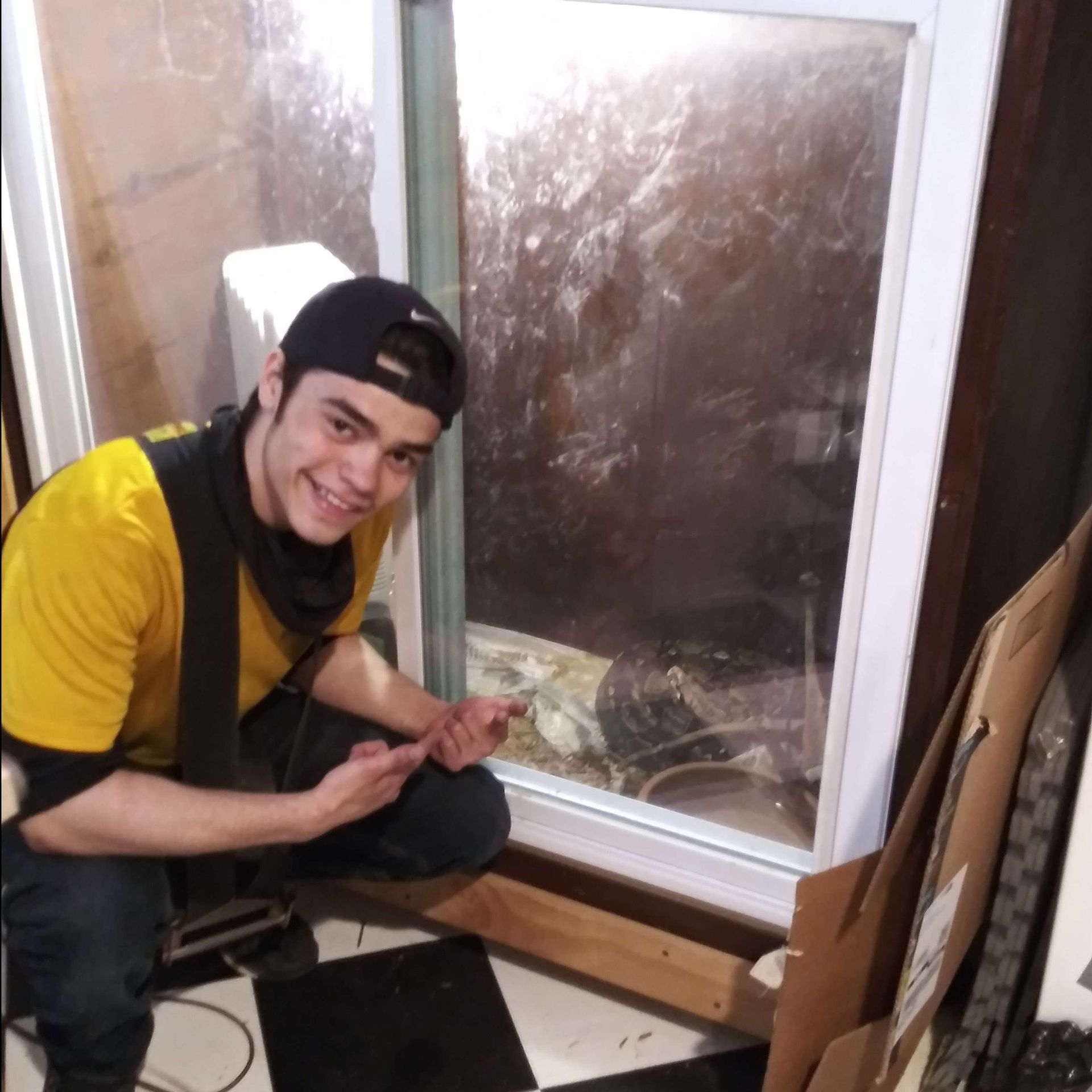 A man in a yellow shirt is kneeling in front of a window