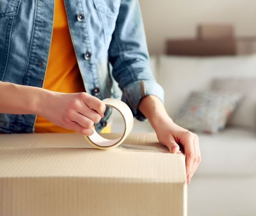 A woman is taping a cardboard box with tape.