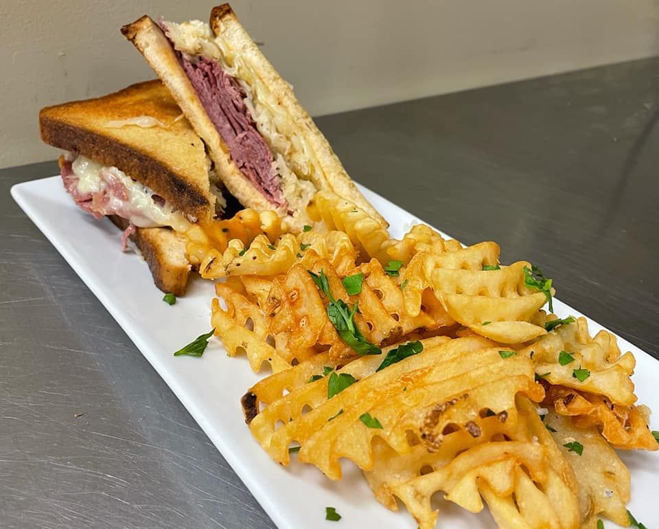 Reuben sandwich with waffle fries on a white rectangular plate; close-up view.