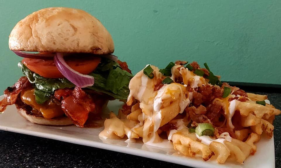 Burger with bacon, lettuce, tomato, and waffle fries with sauce and bacon bits on a white plate.