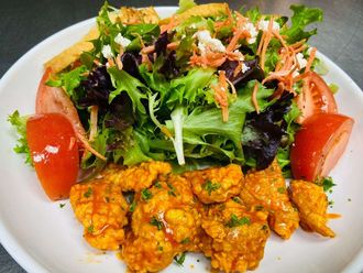 Salad with fried chicken and tomatoes on a white plate.