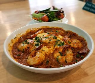 Shrimp and grits in white bowl, topped with parsley, with salad in the background.