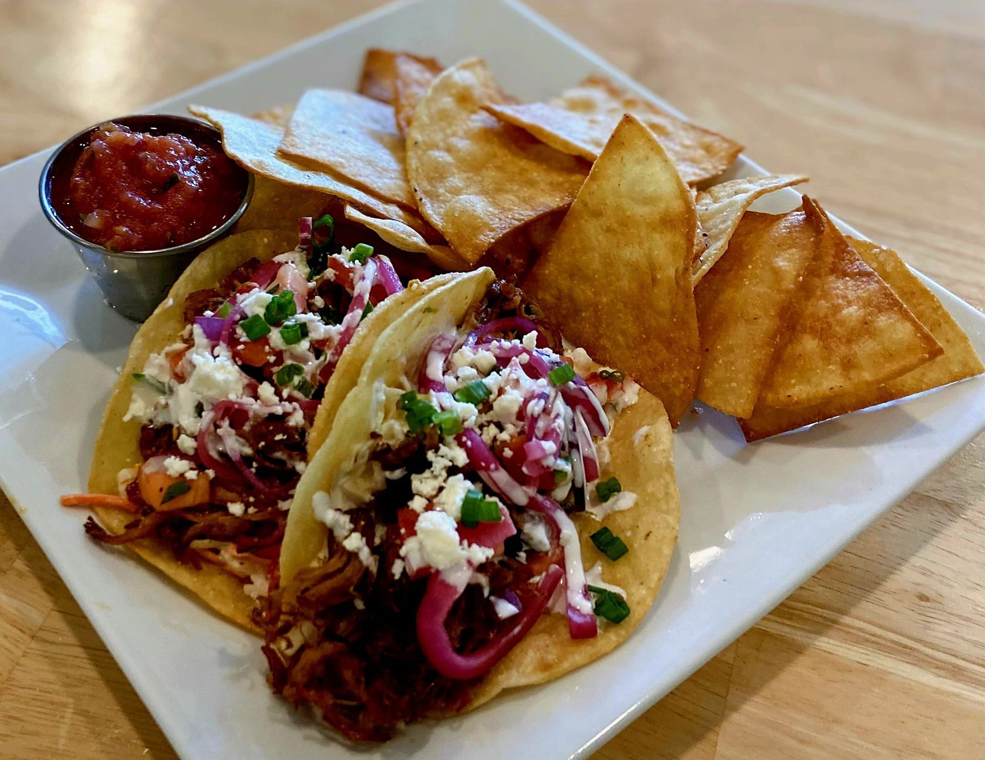 Two tacos with chips and salsa on a white plate.