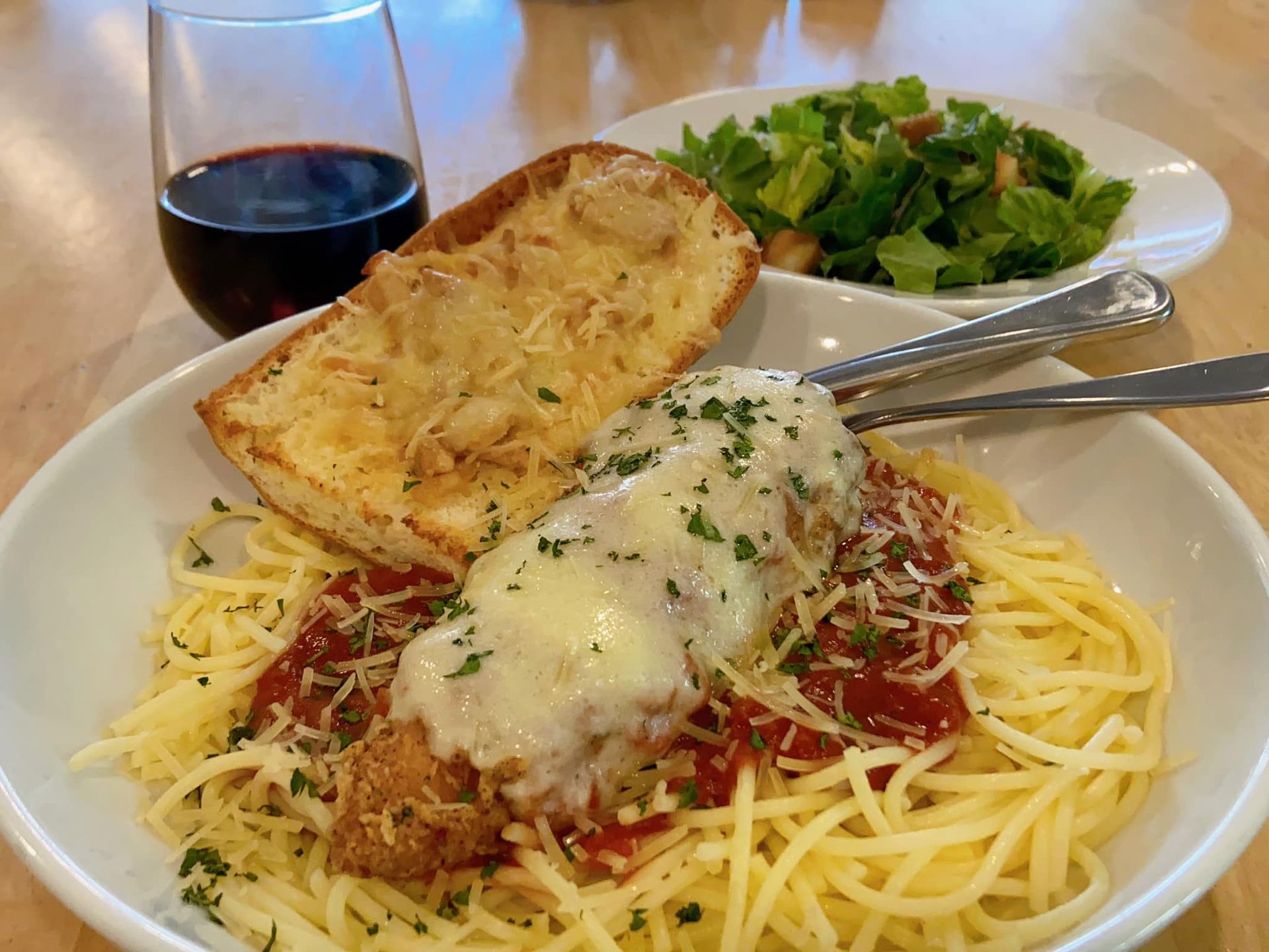 Spaghetti with meatball, garlic bread, salad, and red wine on a table.
