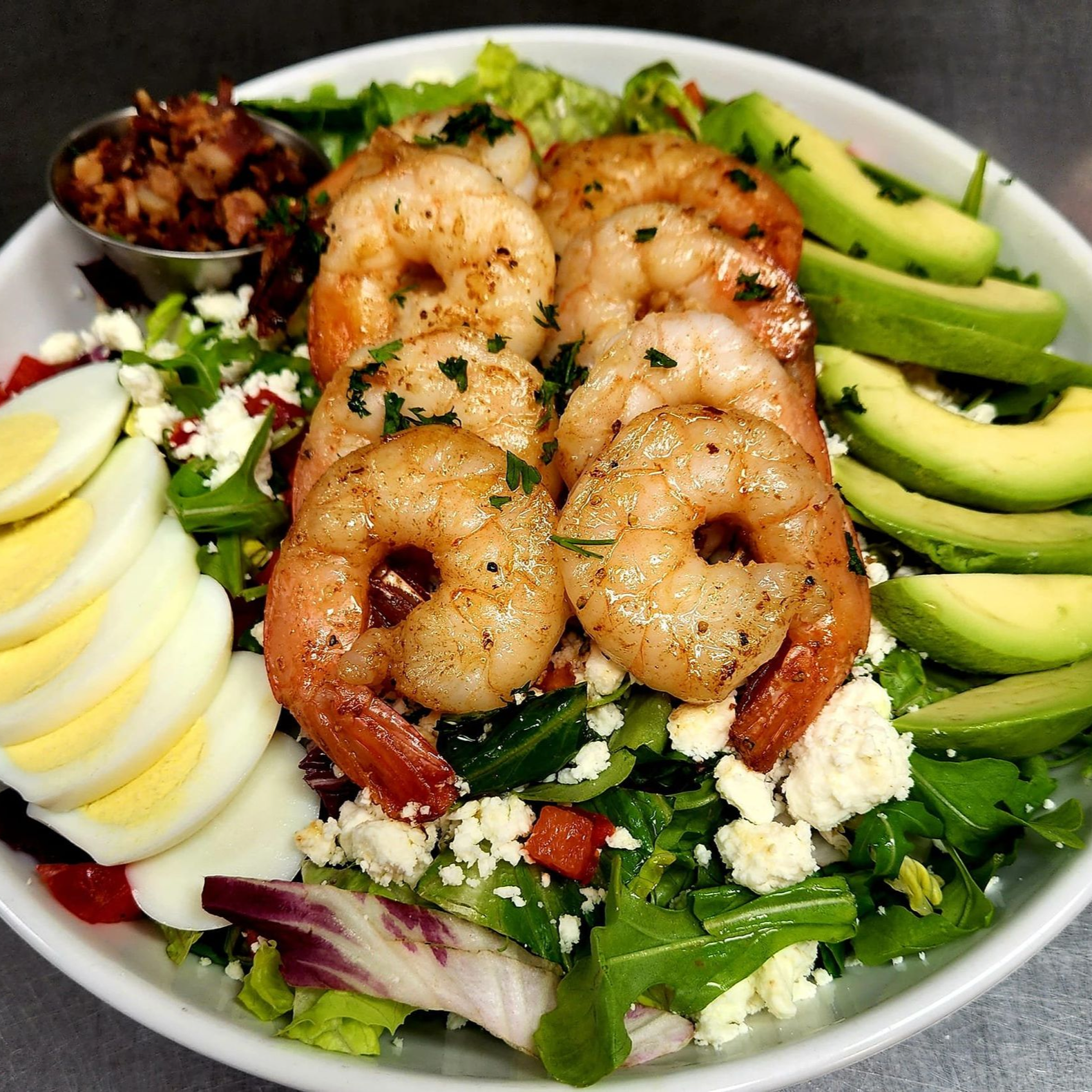 Shrimp salad with avocado, eggs, crumbled cheese, and bacon bits in a white bowl.