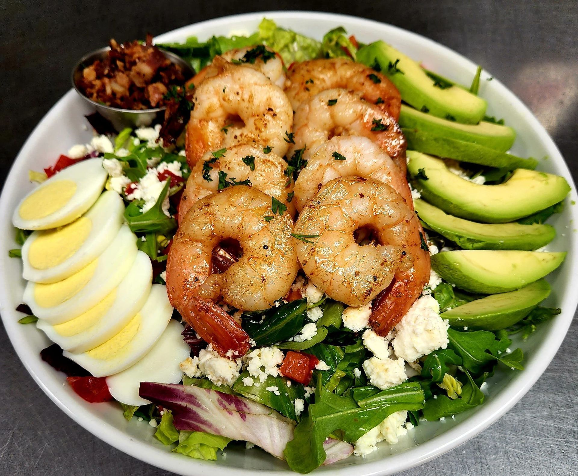 Shrimp salad bowl with avocado slices, hard-boiled egg, feta cheese, and lettuce.