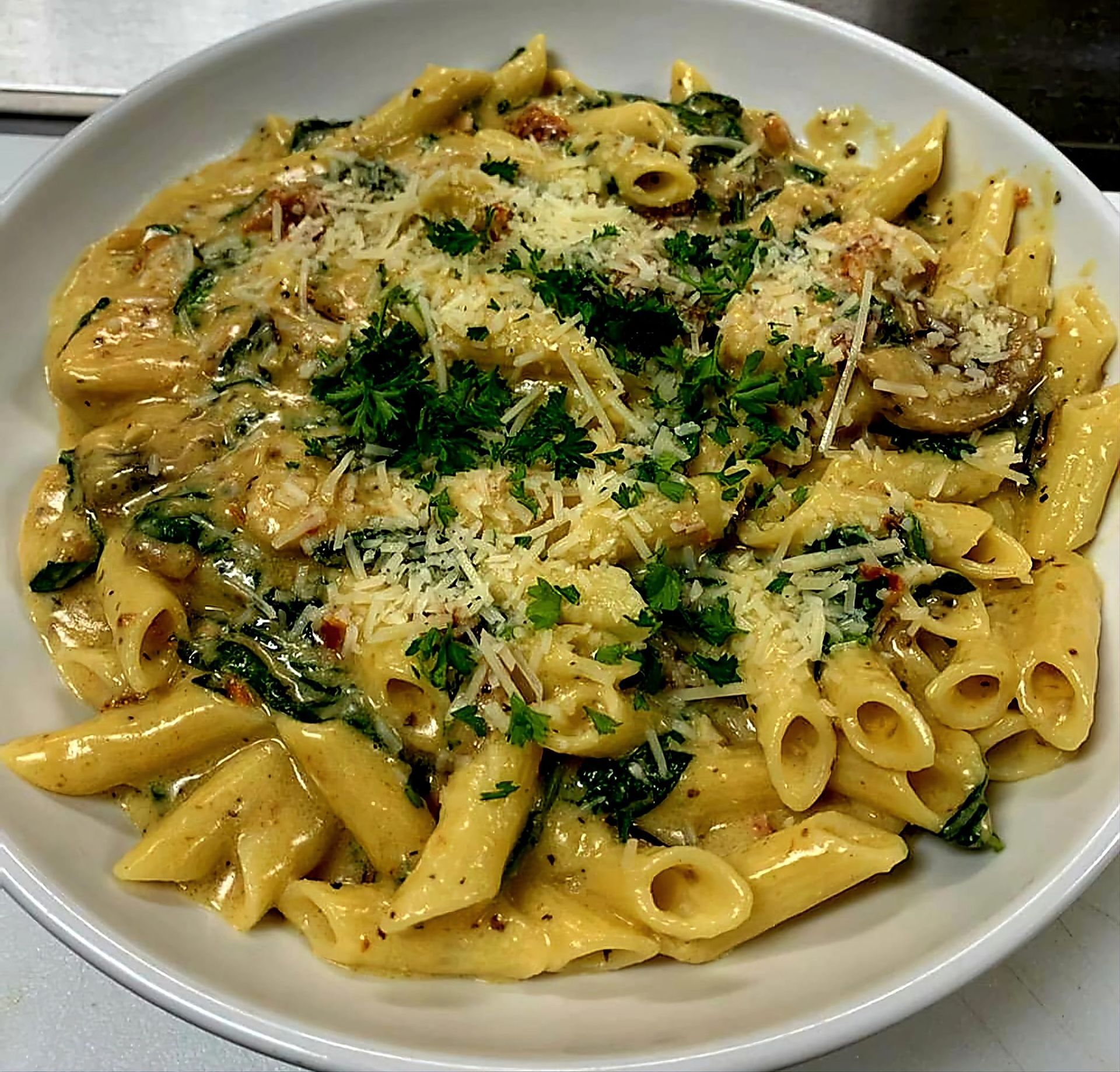 Penne pasta with creamy sauce, spinach, mushrooms, and grated cheese in a white bowl.