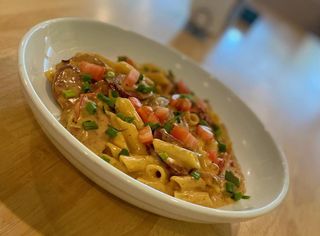 Pasta dish with creamy sauce, tomatoes, and herbs in a white bowl on a wooden table.