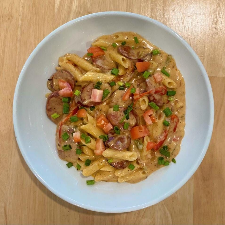 Pasta dish with sausage, tomatoes, and green onions in a creamy sauce, in a blue bowl.