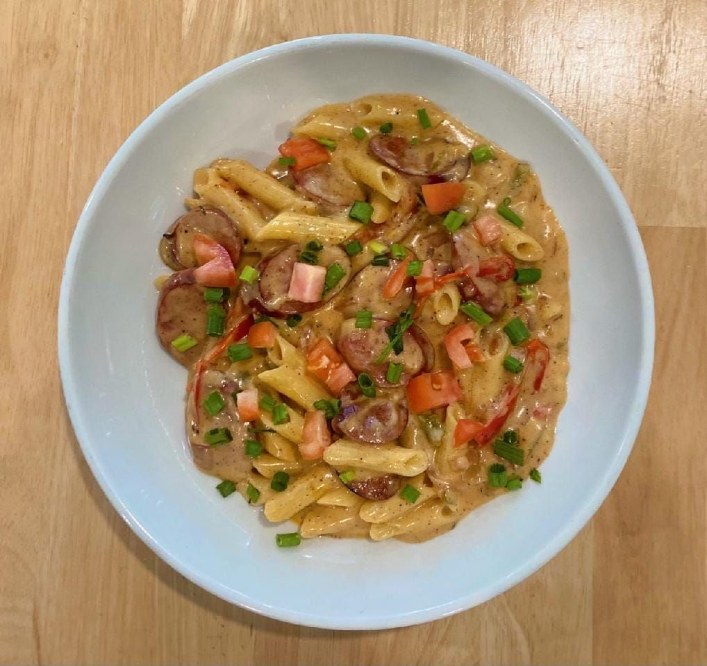 Pasta dish in a bowl with sausage, tomatoes, and green onions.