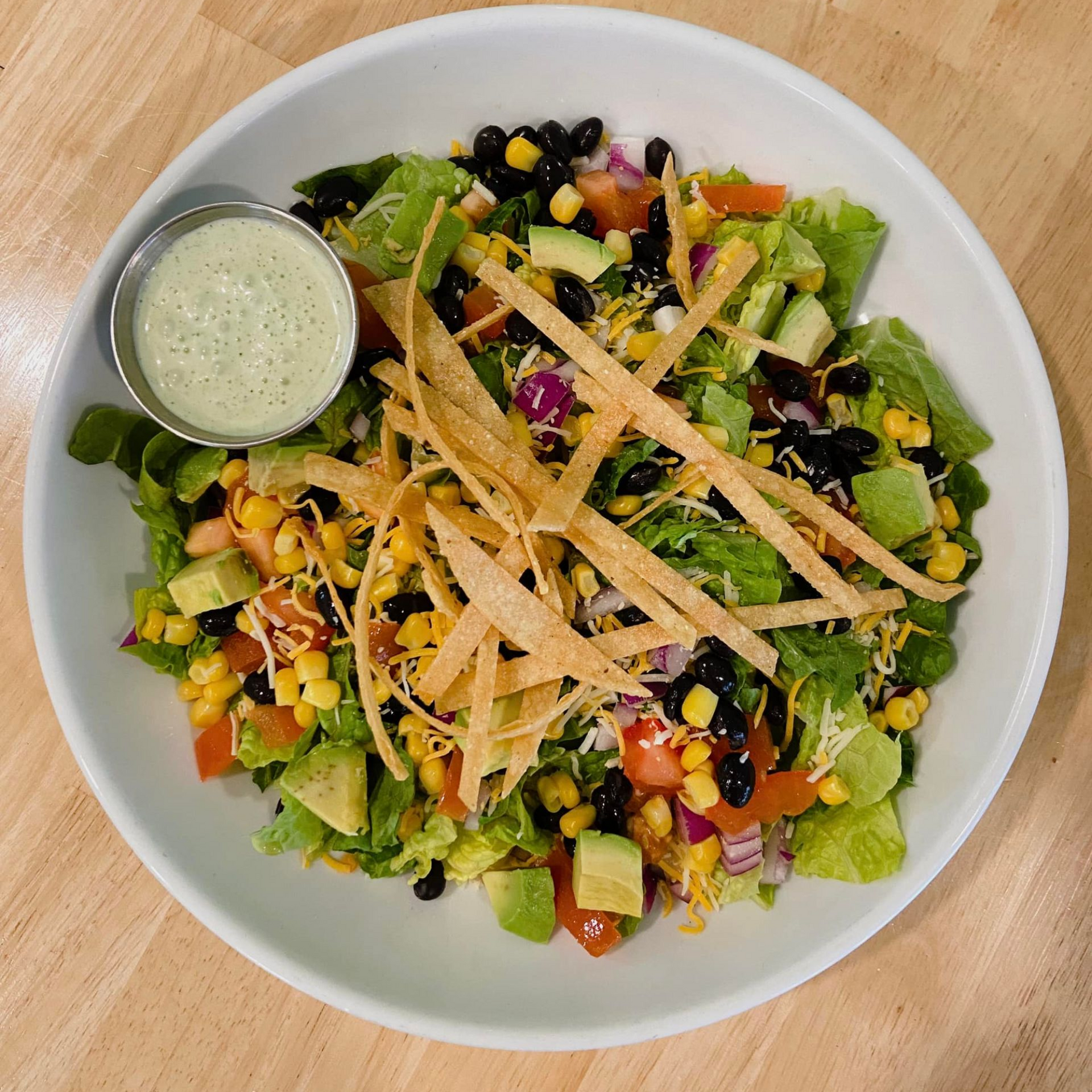 Salad with romaine lettuce, avocado, black beans, corn, tomatoes, tortilla strips, and dressing.