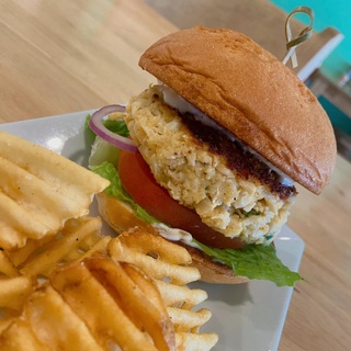 Burger with waffle fries on a white plate. Red onion, tomato, and lettuce with a bun.