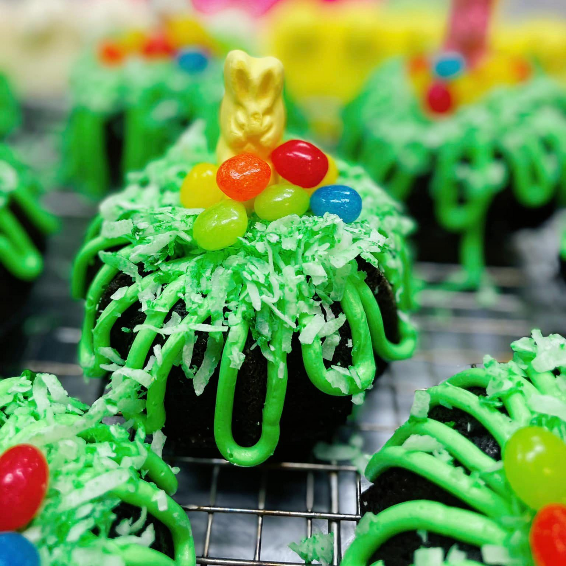 Close-up of chocolate cupcakes with green frosting, coconut flakes, jelly beans, and a gummy bear.