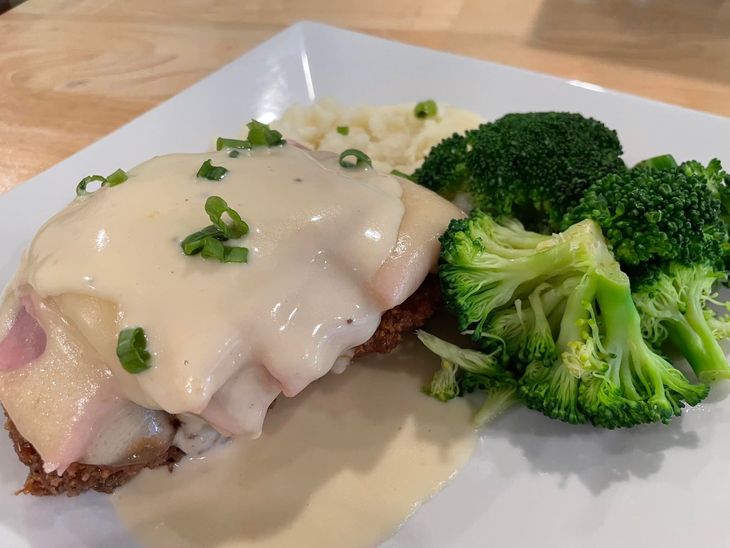Chicken cordon bleu with gravy, broccoli, and mashed potatoes on a white plate.