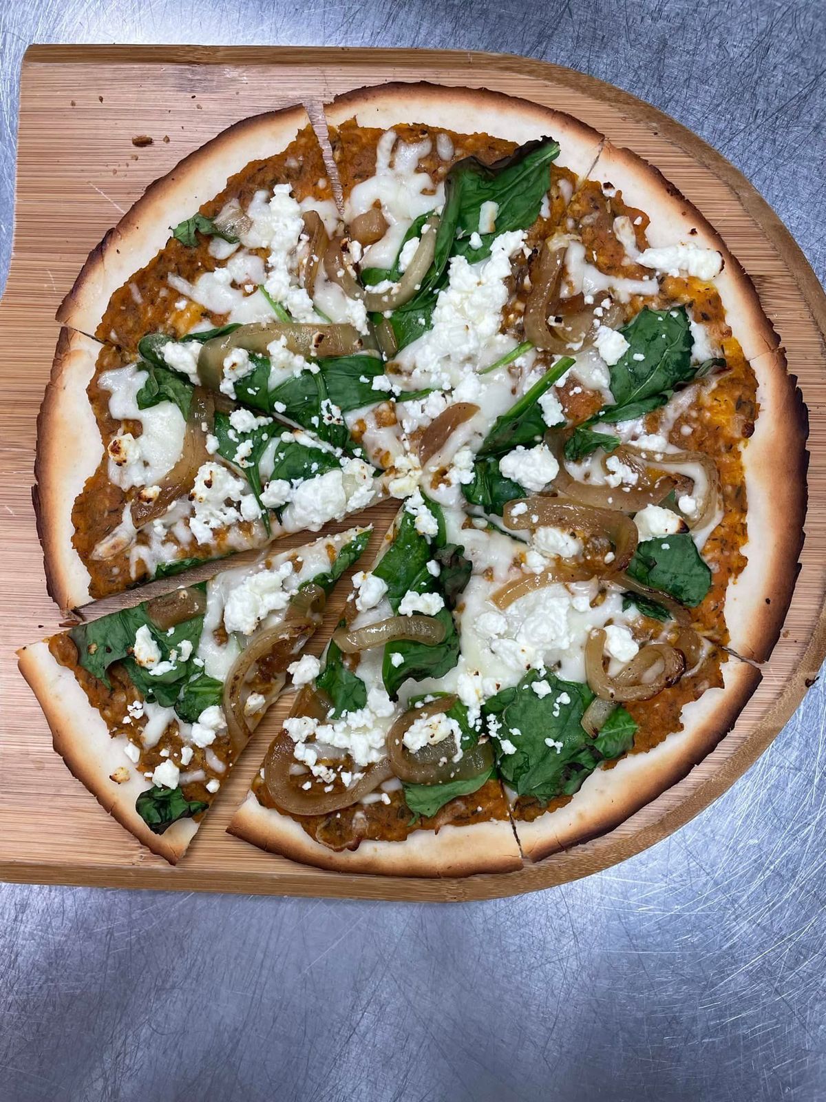 Pizza with butternut squash sauce, spinach, caramelized onions, and feta on a wooden board.
