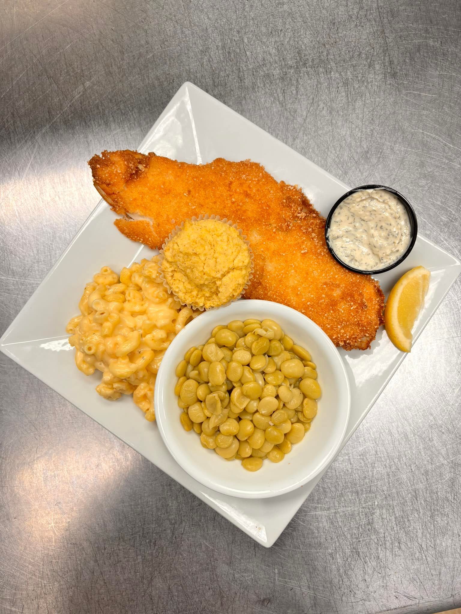 Fried fish fillet with sides of mac and cheese, beans, cornbread, and tartar sauce.